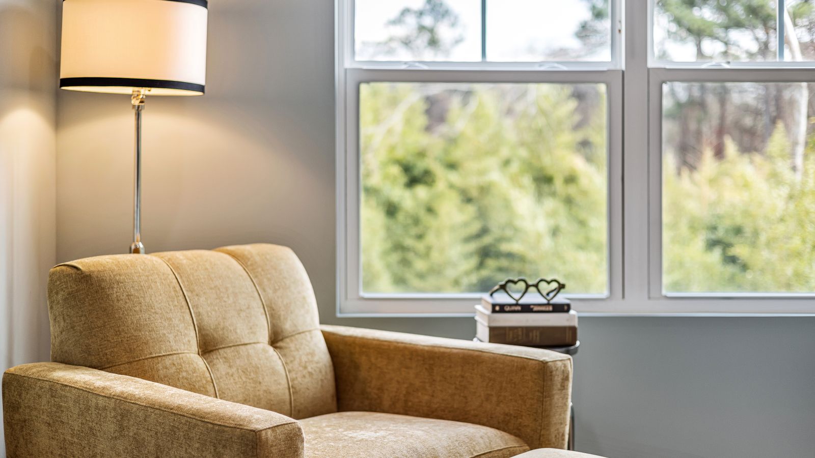 A single armchair beside a window with a tall lamp and a stack of books, a quiet corner in an empty nest