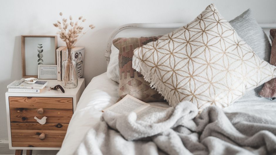 Bed with two linen sleeping pillows, two oatmeal euro shams and one lumbar pillow arranged in three rows under warm sconce light