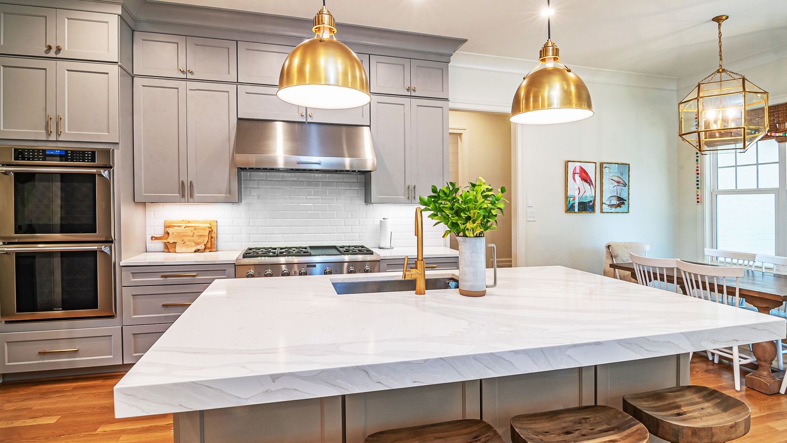 Three brass pendant lights glowing warm 2700K over a white marble kitchen island at dusk
